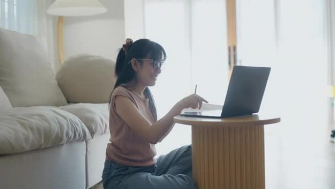 亚洲妇女在用笔记本电脑坐在地板上处理文件。