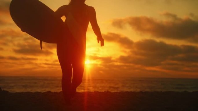 有着棕色长发的女人，在日落时，她的冲浪板在手臂下从海边走到海滩