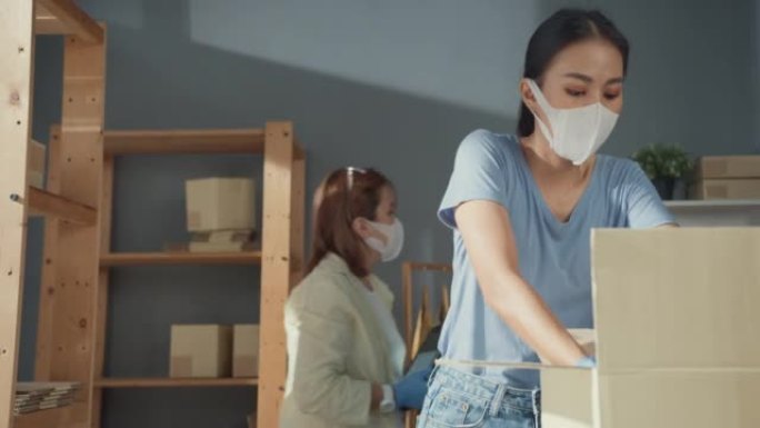 专业两位亚洲女士休闲服防护手套外科口罩持有平板电脑检查库存准备包装衬衫产品发送客户。新型冠状病毒肺炎