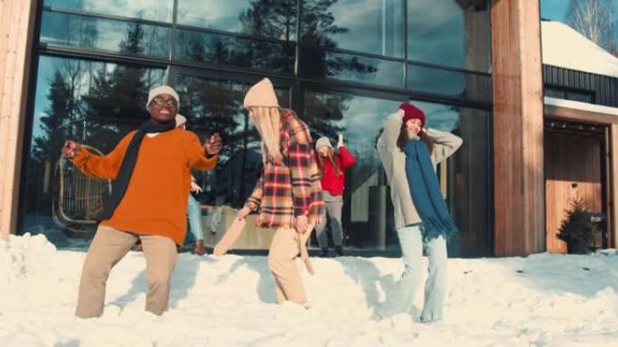 一群快乐的多民族年轻朋友在阳光明媚的雪屋露台慢动作一起跳舞庆祝新年。