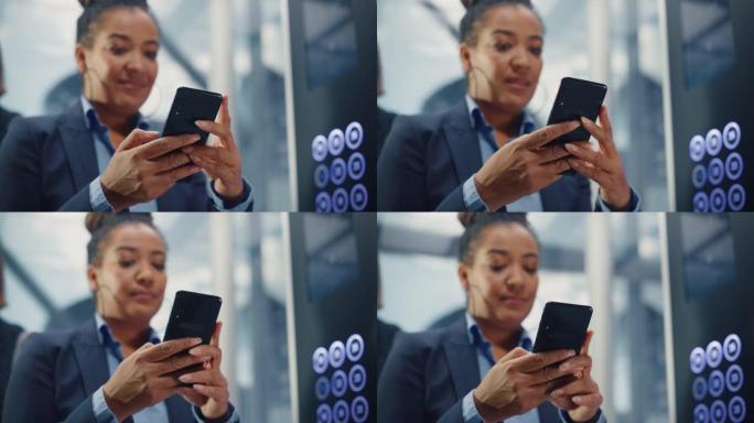 黑人成年女性乘坐拥挤的玻璃电梯到商务中心办公室的特写镜头。成功的非洲裔美国经理使用智能手机，在电梯里