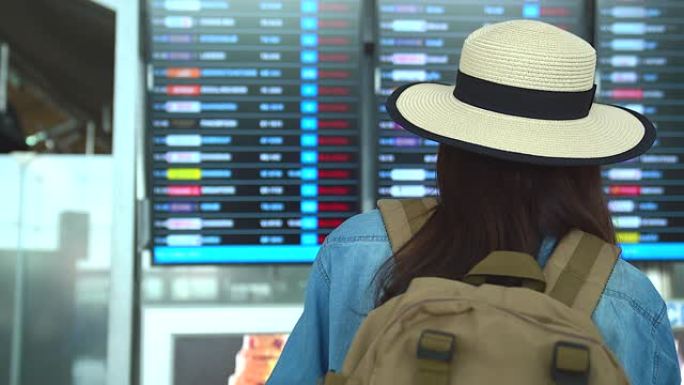穿着旅游服装的美丽亚洲女人看板关于航班时刻表的信息。出国旅行可以用于代表独自旅行的概念工作中。