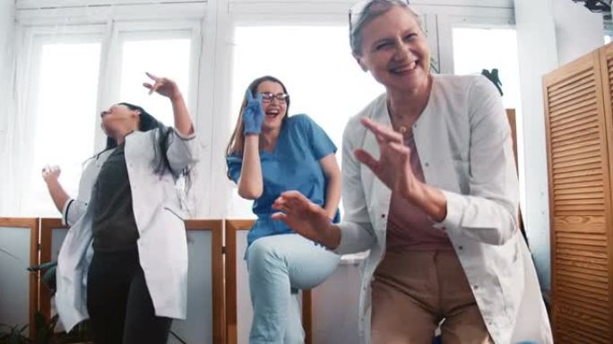 战斗冠状病毒结束。缩小三个有趣的多民族快乐的女医生在诊所实验室办公室一起跳舞。