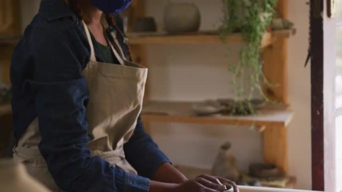 戴着口罩和围裙的女陶工在陶艺工作室的陶艺轮上制作陶器