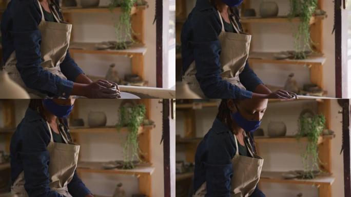 戴着口罩和围裙的女陶工在陶艺工作室的陶艺轮上制作陶器