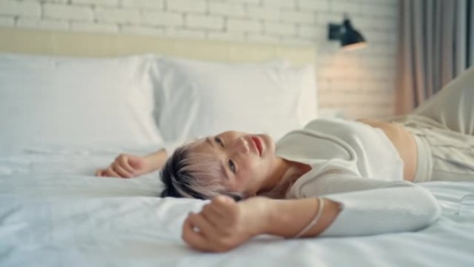 疲惫的亚洲女人在酒店房间里用柔软的床享受。