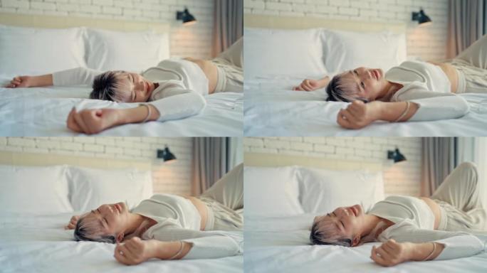 疲惫的亚洲女人在酒店房间里用柔软的床享受。