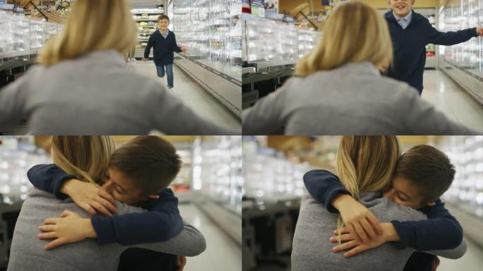 一个快乐微笑的儿子的真实镜头正在奔跑，给他的母亲一个有效的拥抱和亲吻，同时在超市一起购物。
