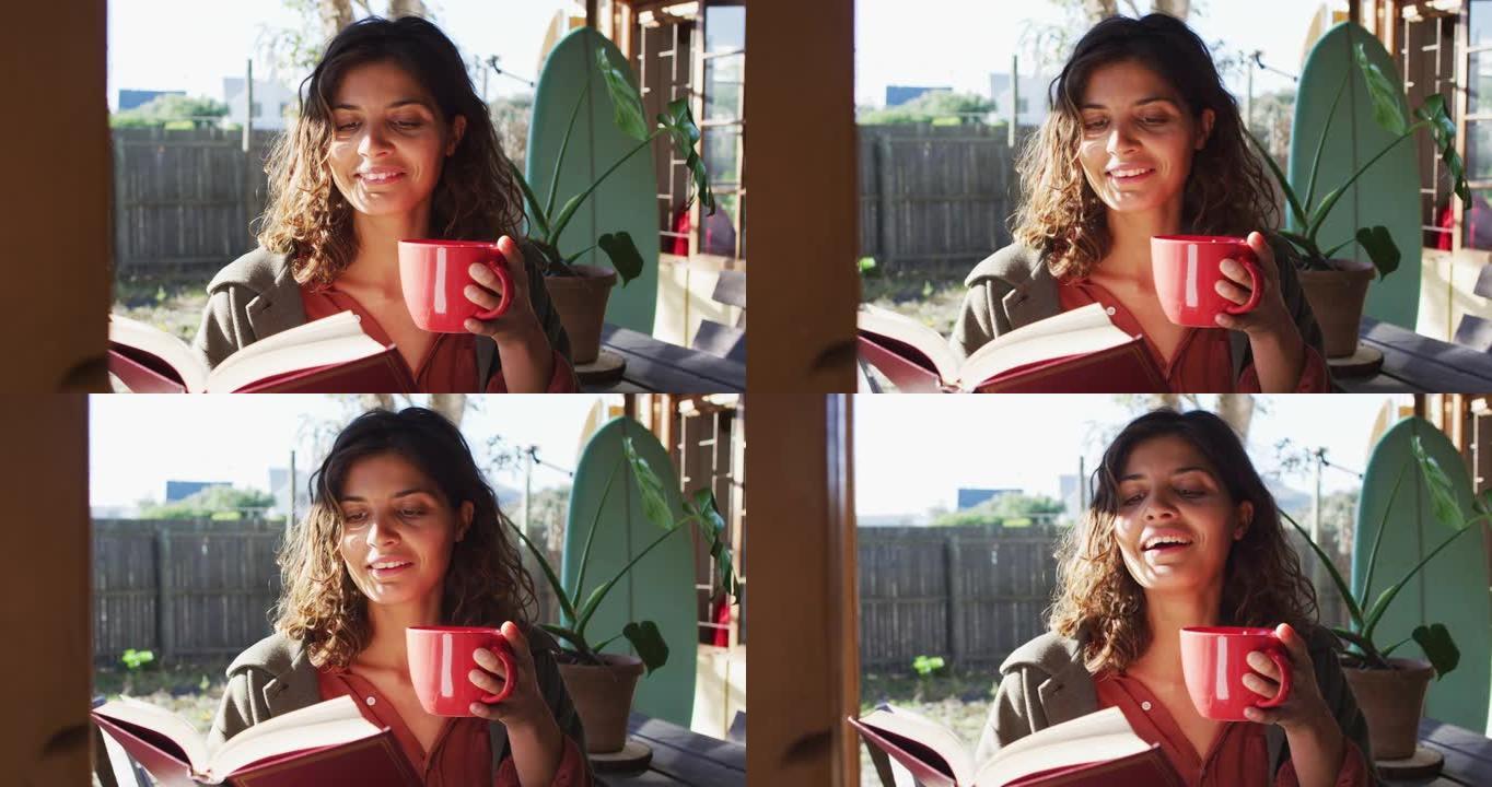 快乐的混血女人坐在阳光明媚的小屋厨房喝茶看书