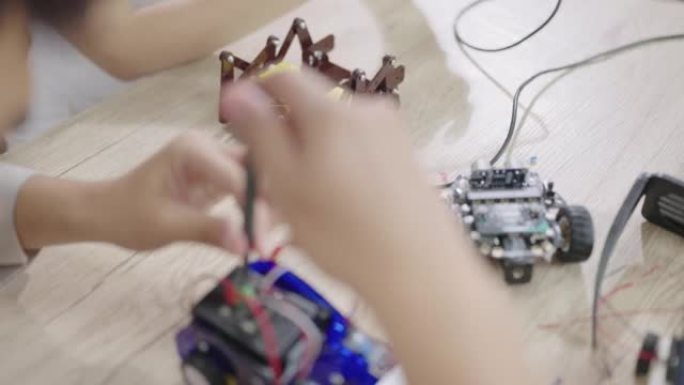 一名高中生正在使用螺丝刀修理机器人汽车，另一名学生正在使用操纵杆控制蜘蛛腿机器人汽车。