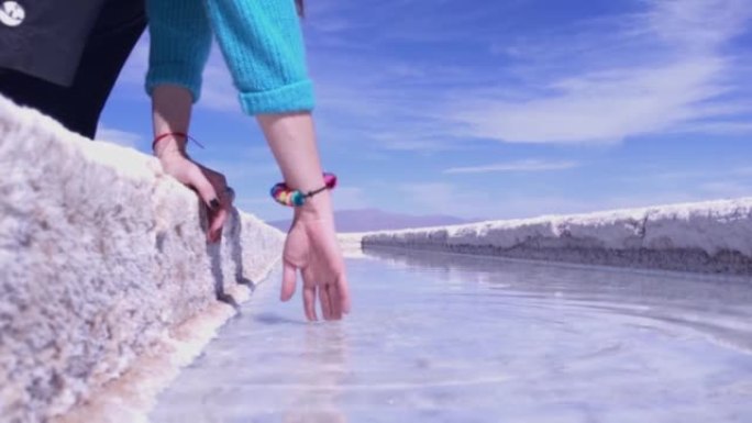 妇女在阿根廷胡胡伊省萨利纳斯·格兰德斯盐滩的盐池里触摸盐水。特写。