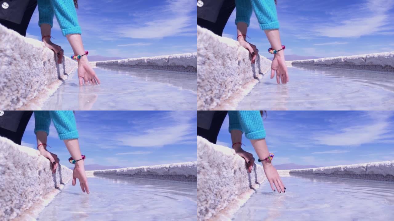 妇女在阿根廷胡胡伊省萨利纳斯·格兰德斯盐滩的盐池里触摸盐水。特写。