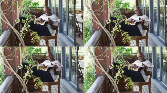 体贴的非洲裔美国老人坐在阳台上弹奏原声吉他