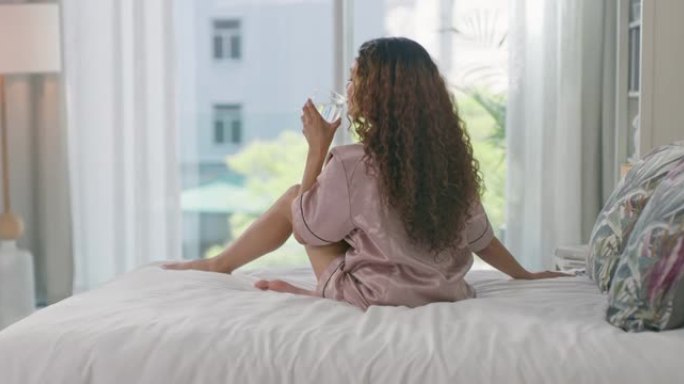 4k视频片段，一名年轻女子在床上放松并在家喝咖啡