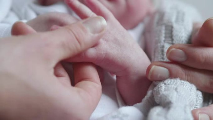 新妈妈的真实特写镜头早上在卧室里抚摸着她刚出生的婴儿的手。