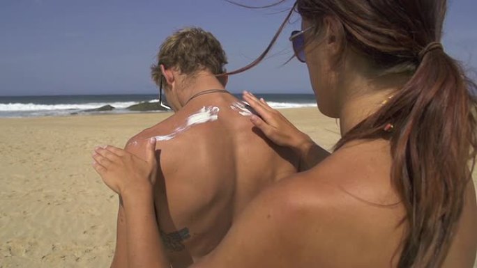 女人在男朋友的背上涂上防晒霜