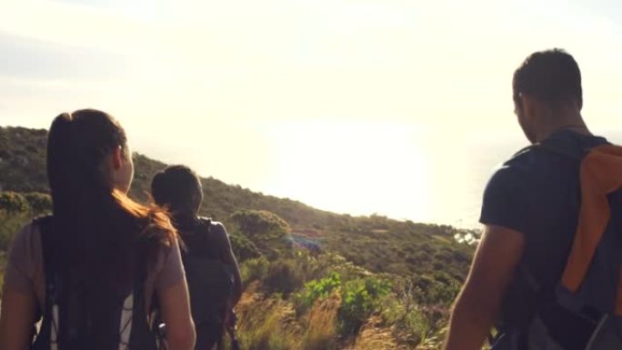 徒步旅行者在阳光下用登山杖走下山路的后视。一群积极冒险的朋友在沿海探索一条小路。游客在户外享受风景秀
