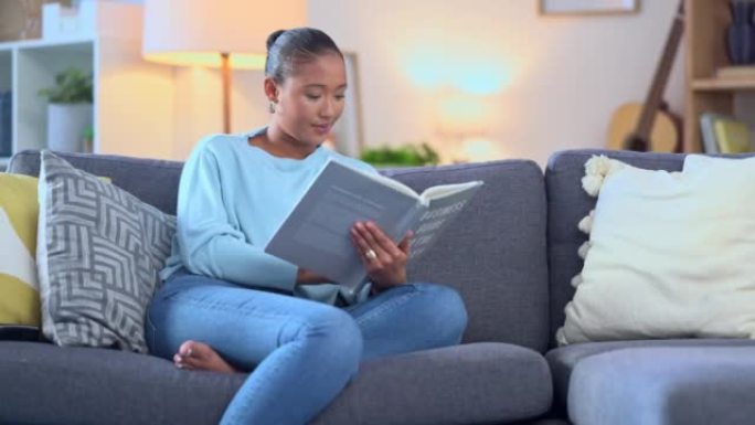 年轻女子在家看书或小说或学习考试，而坐在沙发上放松。快乐美丽的女学生坐在沙发上，带着课本或学习材料