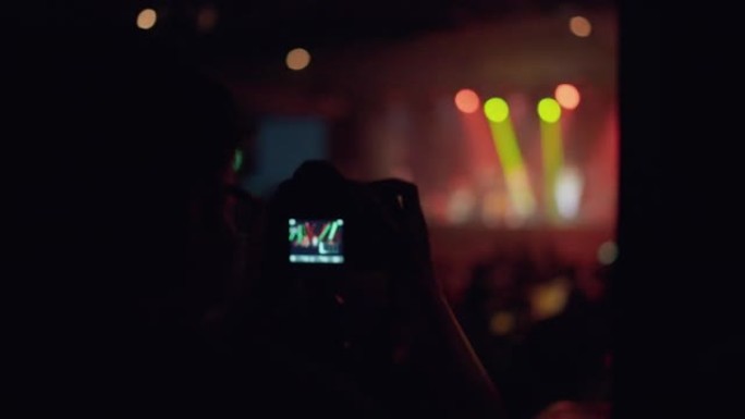 亚洲乐队在舞台上表演音乐会时，男子使用摄像机录制音乐会。