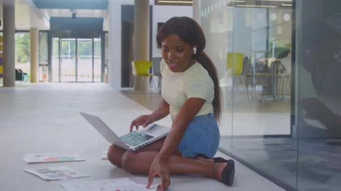 使用笔记本电脑坐在大学大楼地板上的女大学生