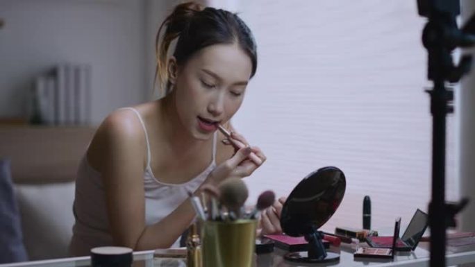 年轻的亚洲女性美容博主拍摄日常化妆常规教程使用三脚架上的手机环形灯