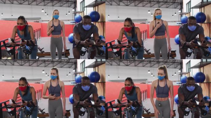 白人女性健身教练在健身房戴着口罩站在固定自行车上