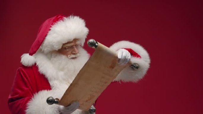 圣诞老人打开纸卷，仔细地看着，微笑着，对他所看到的感到满意，站在红色的背景上