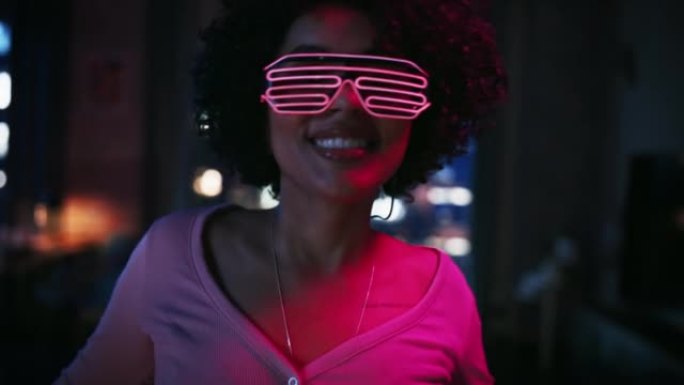 在未来的霓虹灯发光眼镜中跳舞的多民族年轻拉丁女性的特写肖像，在阁楼公寓的家中举行派对。为社交媒体录制