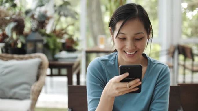 亚洲女孩使用智能手机在咖啡店的桌子上检查互联网上的社交媒体
