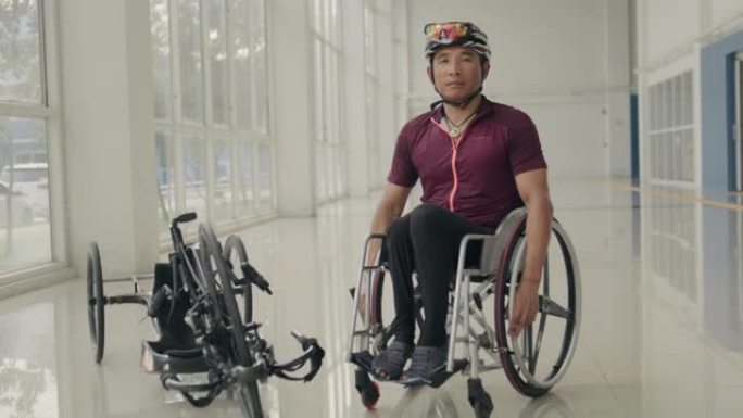 亚洲男子残疾运动员穿着制服，坐在健身房走廊的轮椅上。
