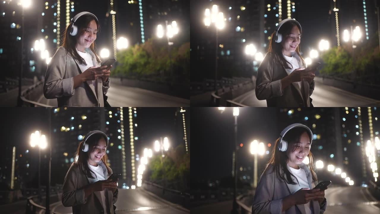 下班后，在城市晚上使用带耳机的智能手机行走的亚洲妇女