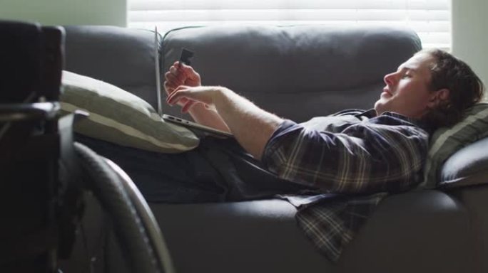 快乐的高加索残疾人躺在客厅的沙发上，使用笔记本电脑