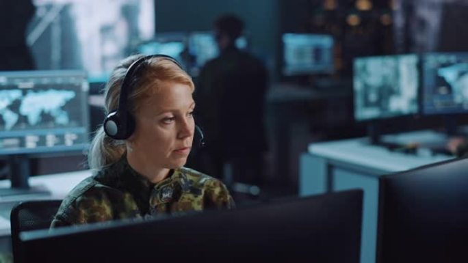 女性军事监视官在中央办公室中心的耳机上交谈，以进行网络操作，控制和监视，以管理国家安全，技术和军队通