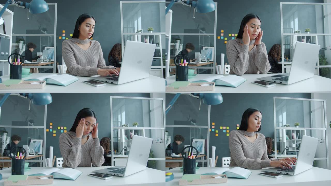 混血女商人使用笔记本电脑然后按摩太阳穴在工作场所感到头痛