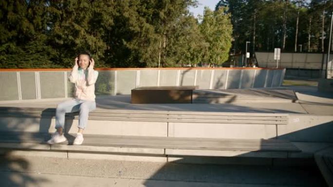 十几岁的女孩坐在操场的长凳上听音乐