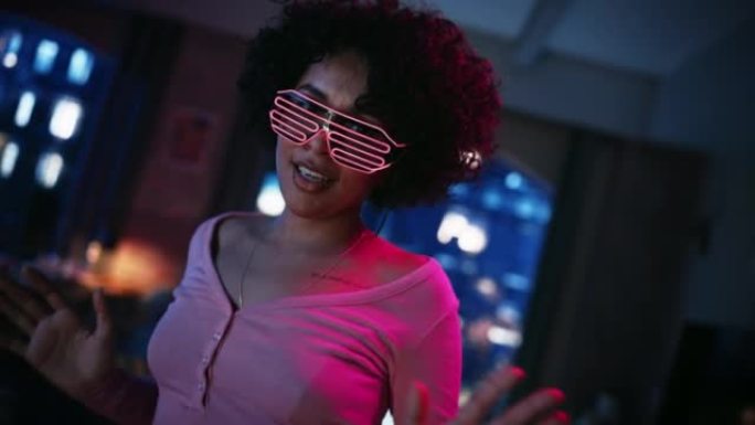 特写多民族年轻黑人女性在未来的霓虹灯发光眼镜中跳舞的肖像，在阁楼公寓的家中举行派对。为社交媒体录制有