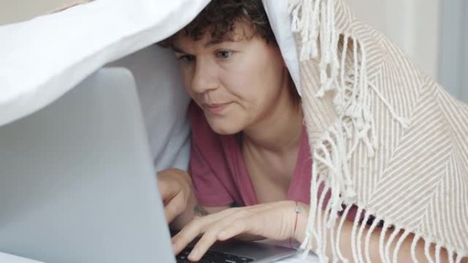 严肃的女孩自由职业者在床上用笔记本电脑工作，专注于工作