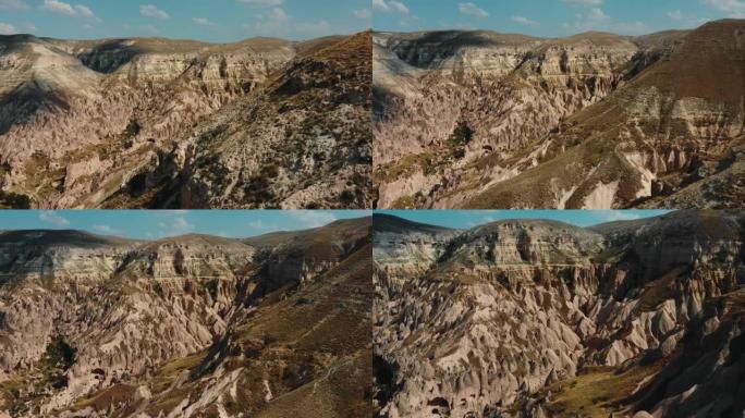 无人机飞越美丽的阳光明媚的山崖，揭示了土耳其卡帕多西亚巨大的灰色岩石景观全景。