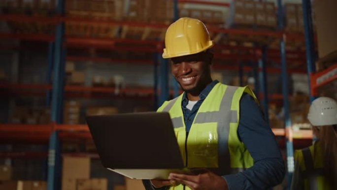专业的男性工人戴着安全帽，拿着笔记本电脑在零售仓库里检查库存和库存，仓库里摆满了货物和工作人员。前视