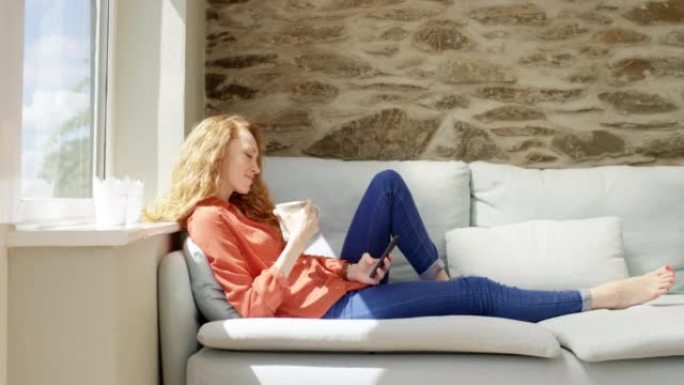 4k视频片段，一名妇女在使用智能手机时喝咖啡