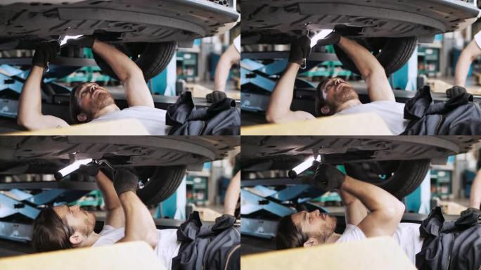英俊的机械师在汽车服务中使用棘轮在汽车下方工作
