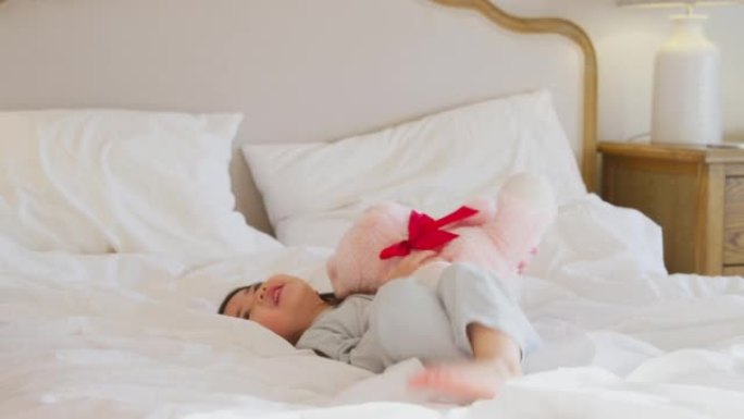 年轻女孩在家穿着睡衣在床上玩耍，拥抱着慢动作拍摄的泰迪熊