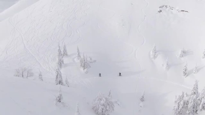 无人机: 参加分板旅行的游客沿着覆盖着粉雪的斜坡跋涉。