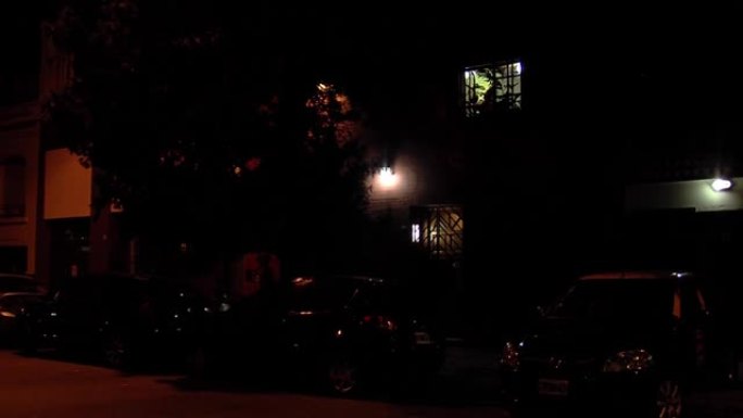 一个女人晚上关上了她家的街窗。放大。