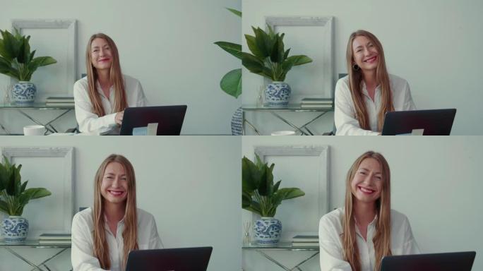 工作中没有压力。用笔记本电脑放大在现代办公室工作的30多岁快乐美丽的女商人，对着相机微笑。
