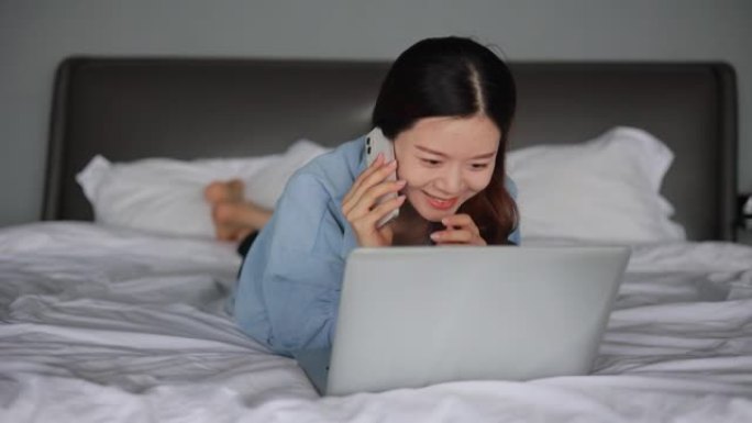 年轻妇女躺在床上使用笔记本电脑并在手机上聊天