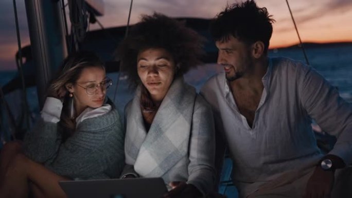 SLO MO三个年轻朋友在黄昏时在帆船甲板上使用笔记本电脑