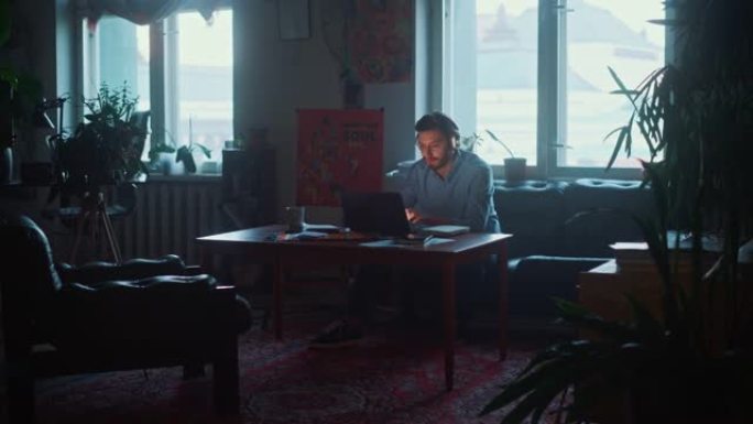 年轻英俊的男人，戴着耳机在创意机构的笔记本电脑上工作，在正宗的阁楼办公室工作。翻新的时尚装饰，配有室