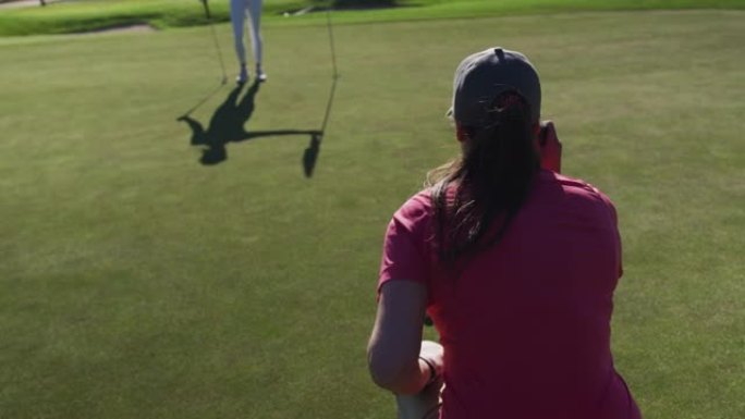 两个白人妇女打高尔夫球一个跪着看球