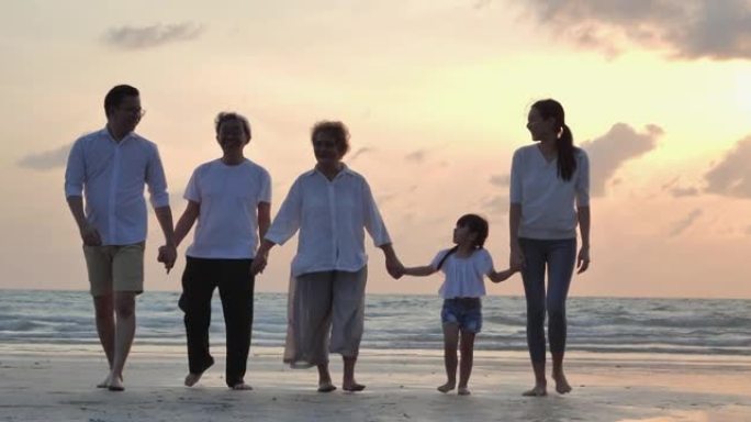 剪影中，快乐的亚洲大家庭五人手牵着手，走向日落海边的沙滩冲浪。幸福在自然的概念。